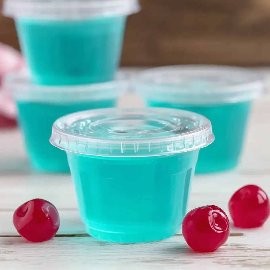 Ein Becher mit blauem Getränk und Kirschen daneben.