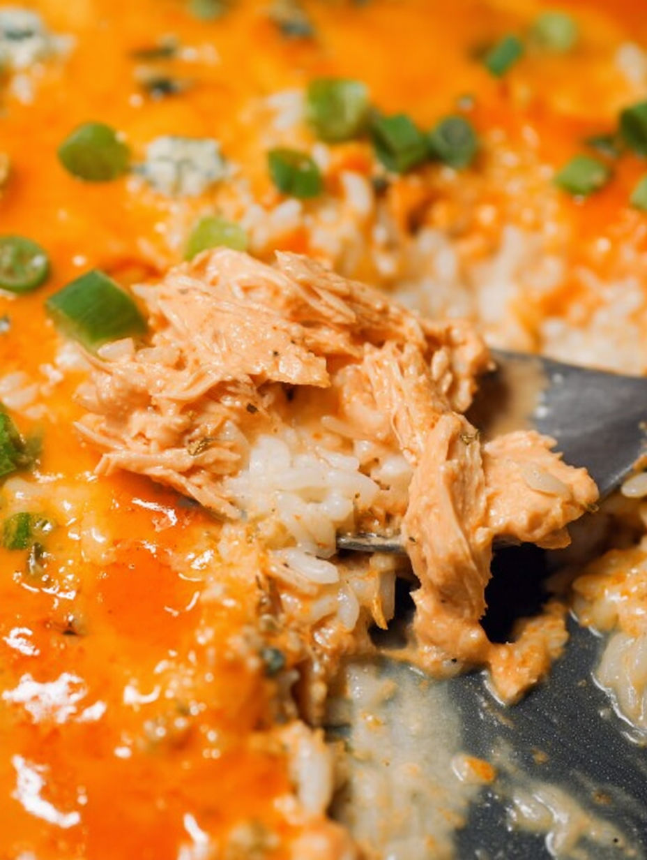 Ein Löffel steckt in einem cremigen Buffalo-Hähnchen-Reisauflauf.