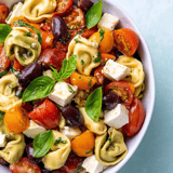 Bunter Nudelsalat mit Tomaten, Oliven und Käse in einer Schüssel.