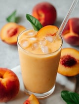 Ein Glas Pfirsichshake mit Eis und Minzblatt.