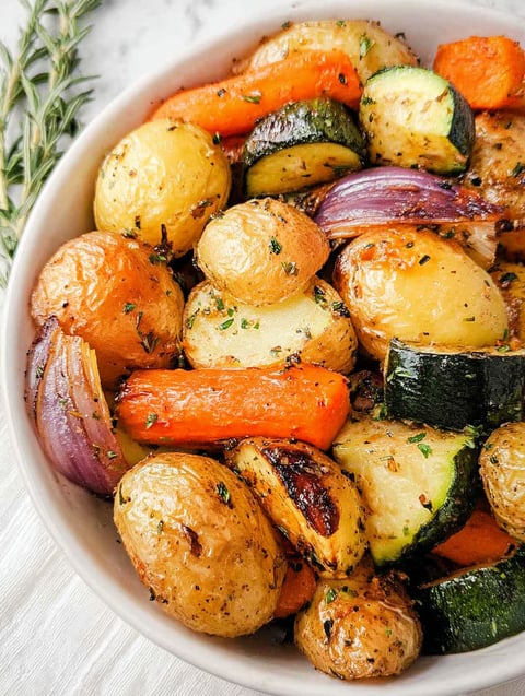 Eine Schüssel mit geröstetem Gemüse wie Kartoffeln, Karotten und Zucchini.