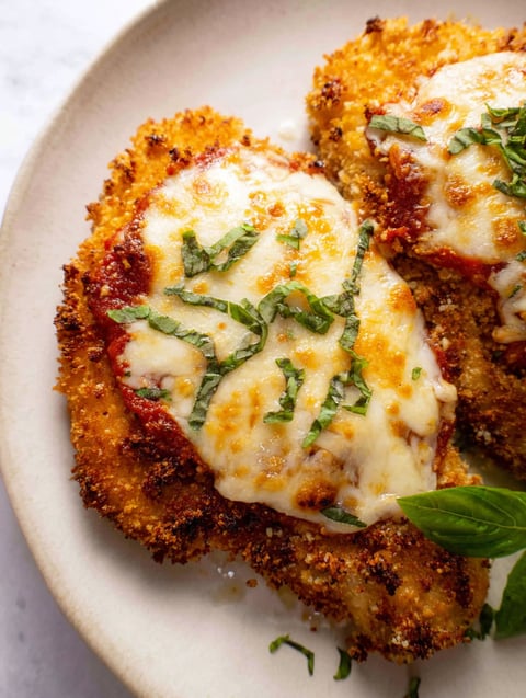 Ein Stück Huhn mit Käse und Kräutern drauf.