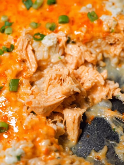 Nahaufnahme von einem Stück Huhn in einem käsigen Buffalo-Huhn-Reis-Auflauf.